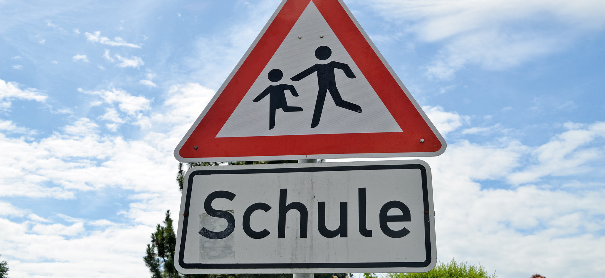 Ein Straßenschild welches vor spielenden Kindern in der Nähe einer Schule aufmerksam macht